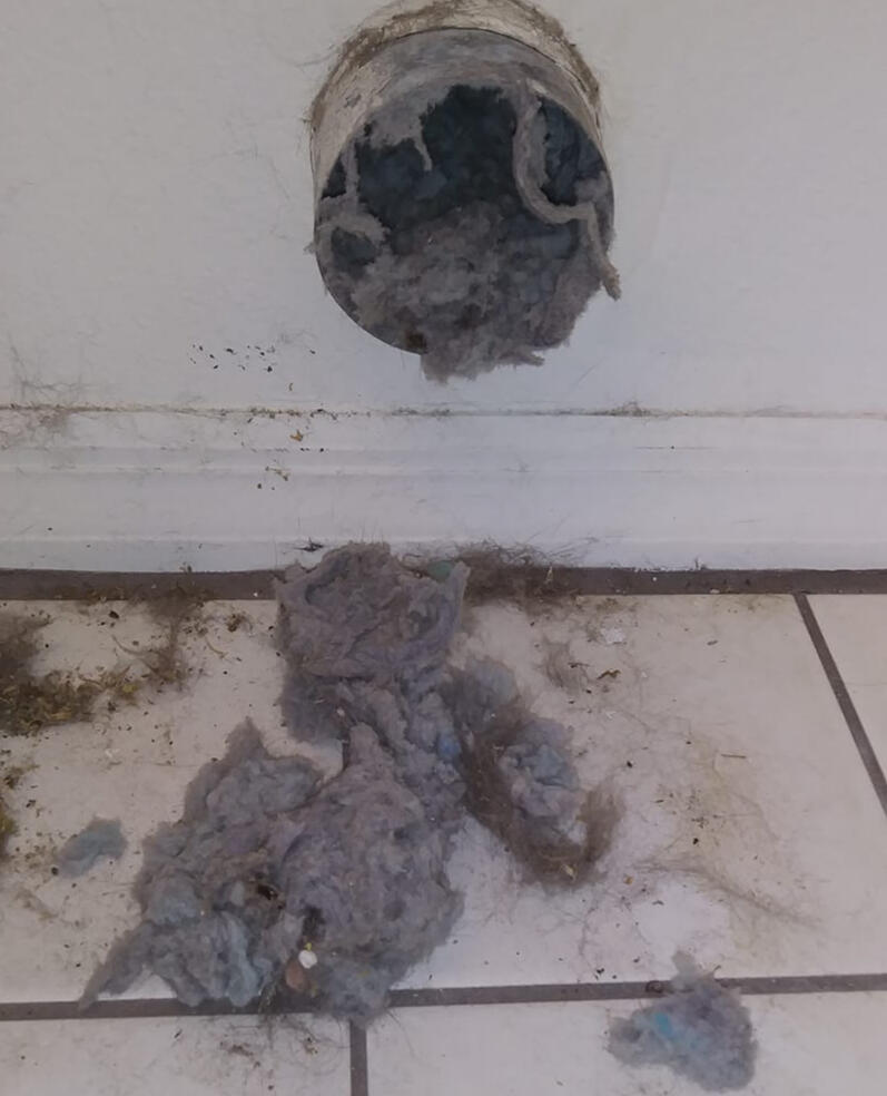 Air vent in wall with lint and dirt falling onto the floor.